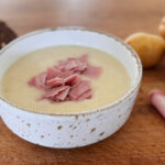 Soupe de pommes de terre crémeuse garnie de fines lanières de jambon fumé, servie chaude dans un bol.