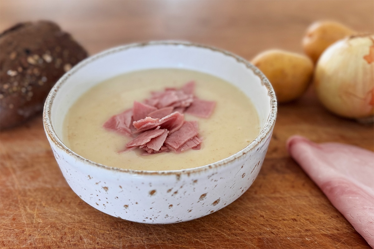 Soupe de pommes de terre crémeuse garnie de fines lanières de jambon fumé, servie chaude dans un bol.